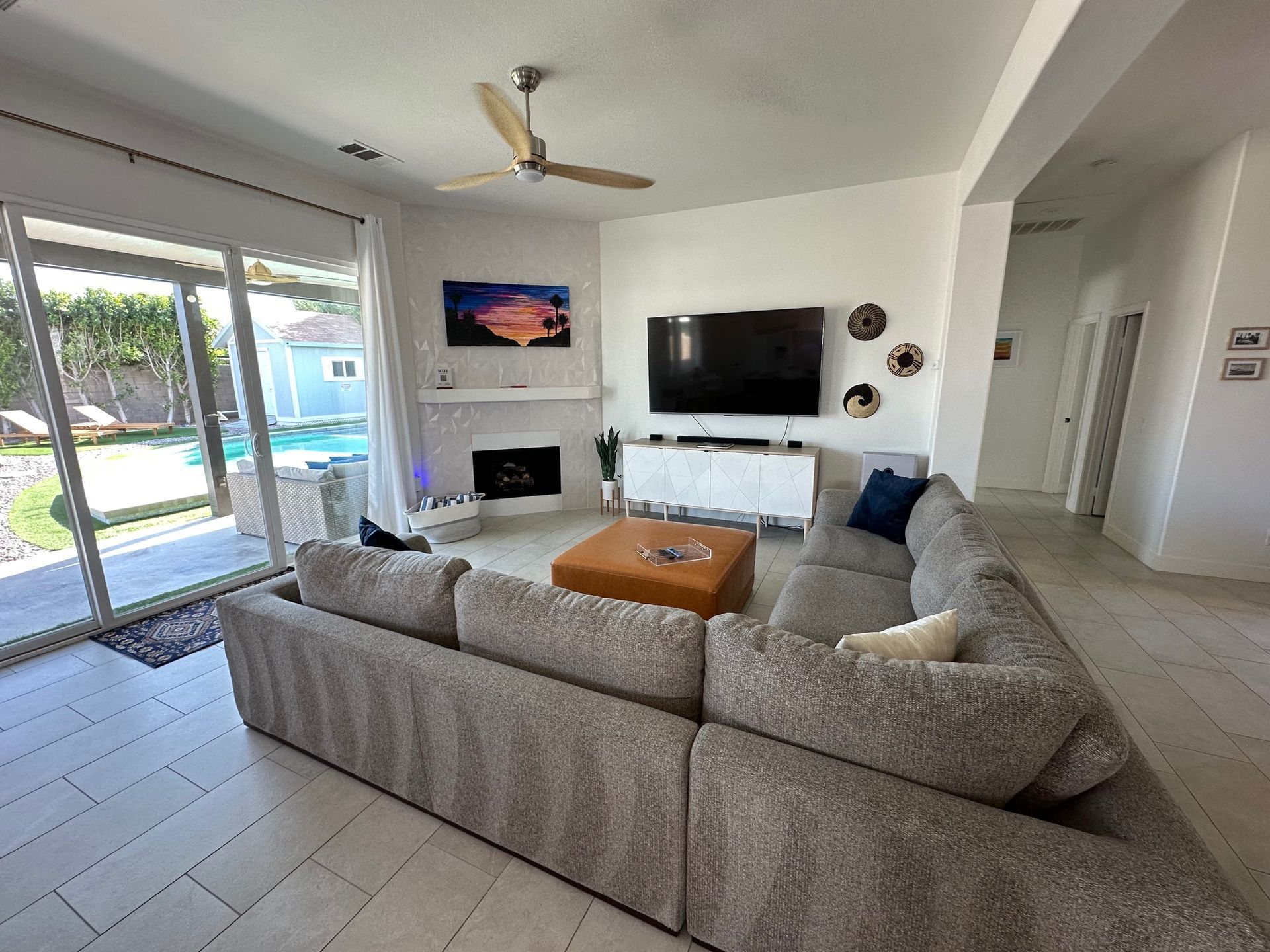 Living room with gray sectional sofa, television, and fireplace, overlooking a pool.