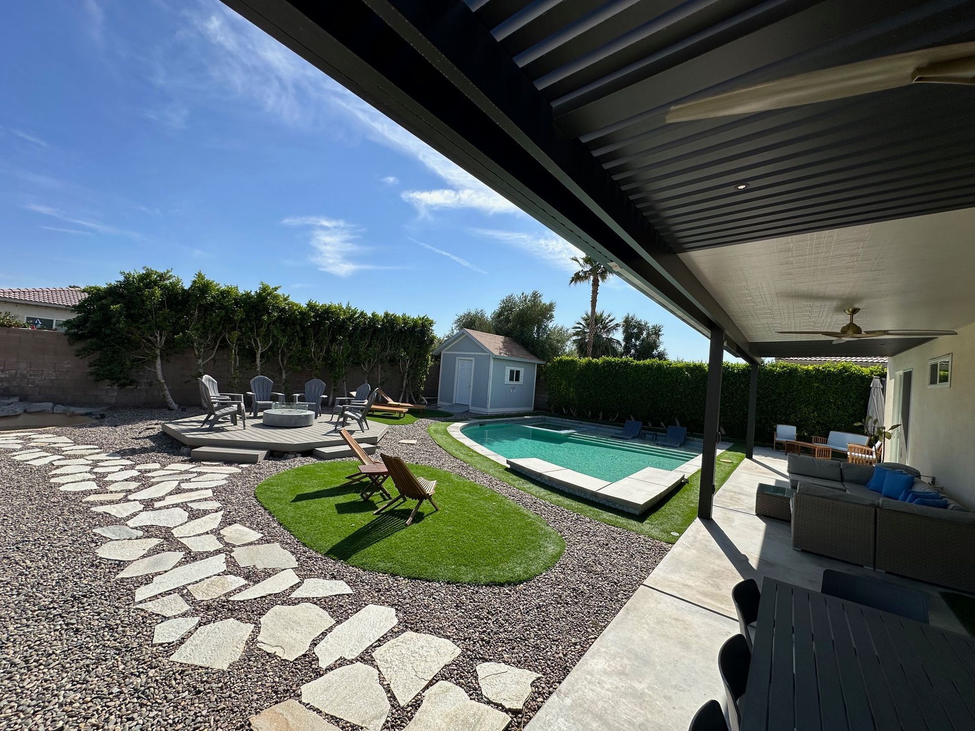 Backyard with pool, patio, fire pit, and shed under a bright blue sky.