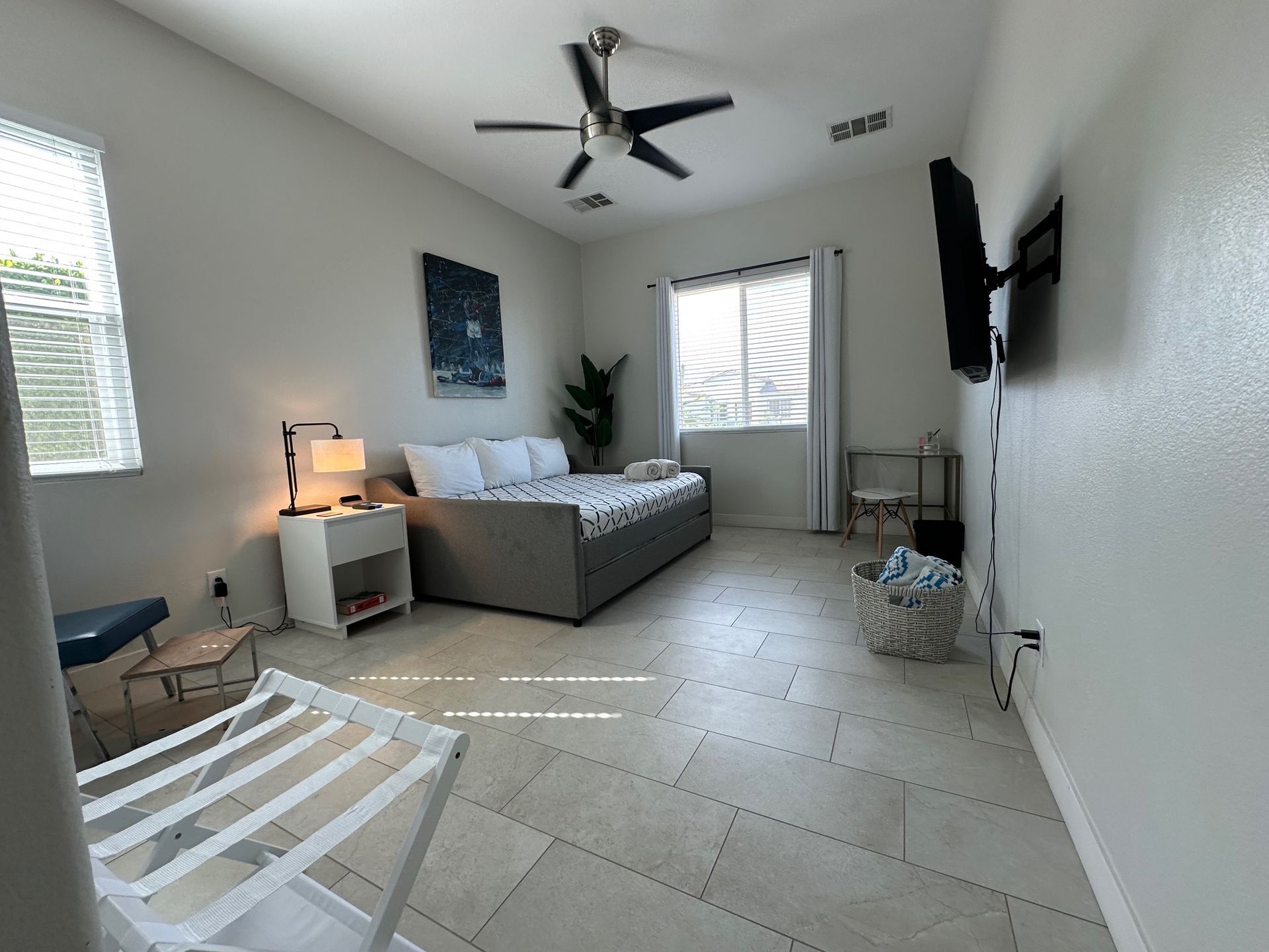 Bright, airy bedroom with a daybed, TV, and luggage rack.