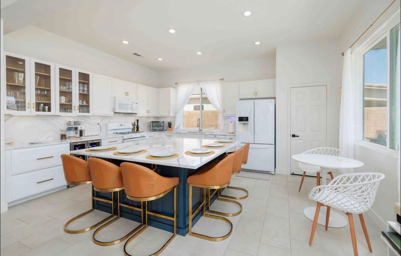 Bright white kitchen with a blue island and orange bar stools