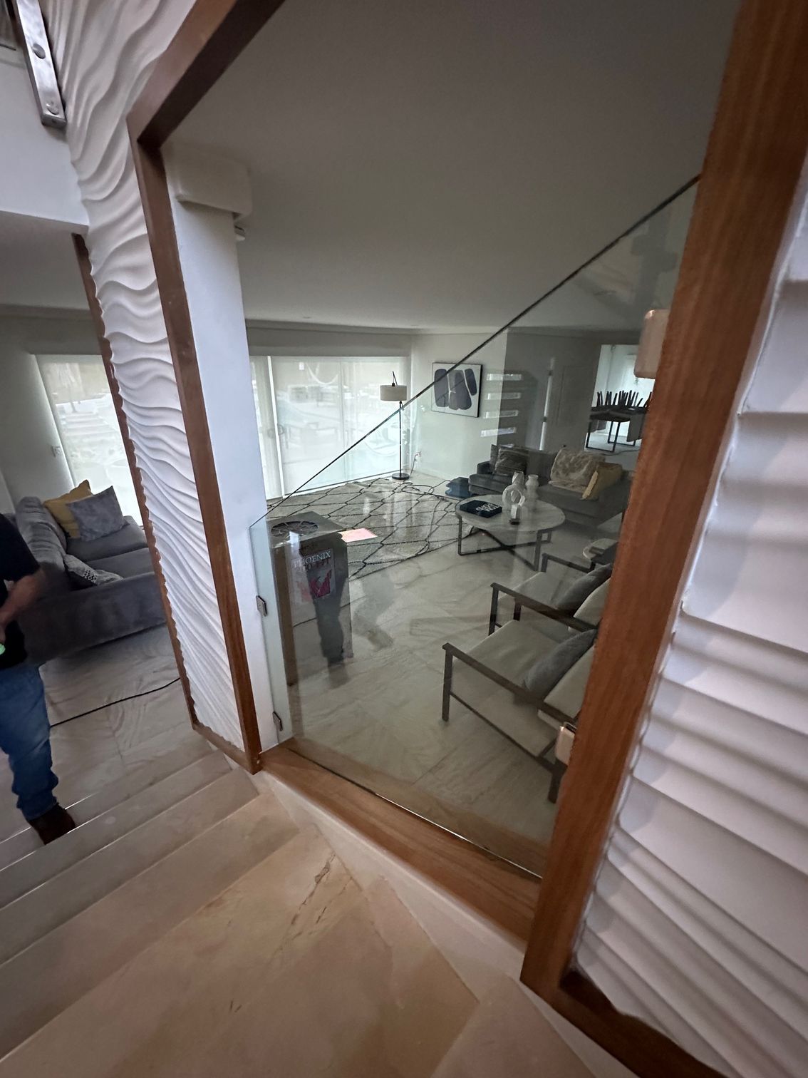 View from a staircase into a room with furniture through a glass panel framed in wood