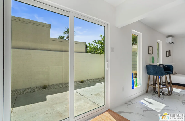 Sliding glass door opens to a concrete patio and a beige wall. Interior has white walls, bar stools.