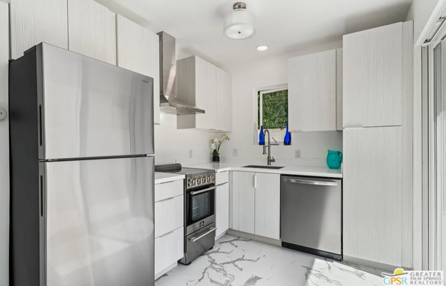 Modern white kitchen with stainless steel appliances, light countertop and cabinet, and patterned flooring.