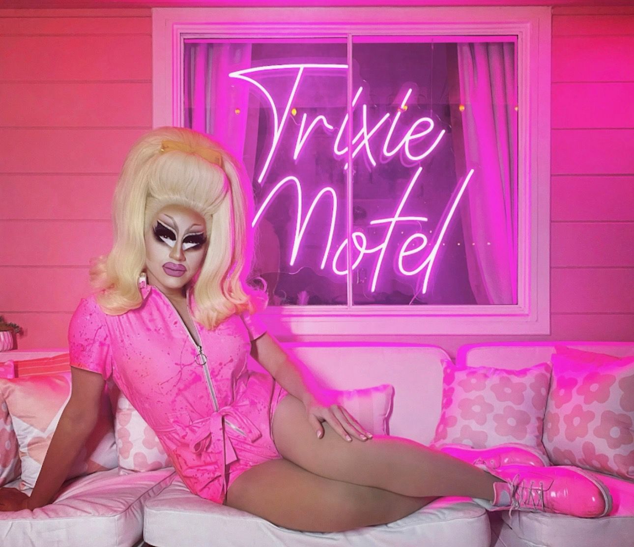 Trixie Mattel in pink outfit, lounging on a white couch.