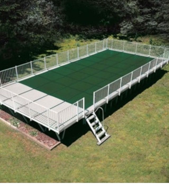 Green rectangular pool on a white deck with a ladder, surrounded by a white fence, in a grassy area.