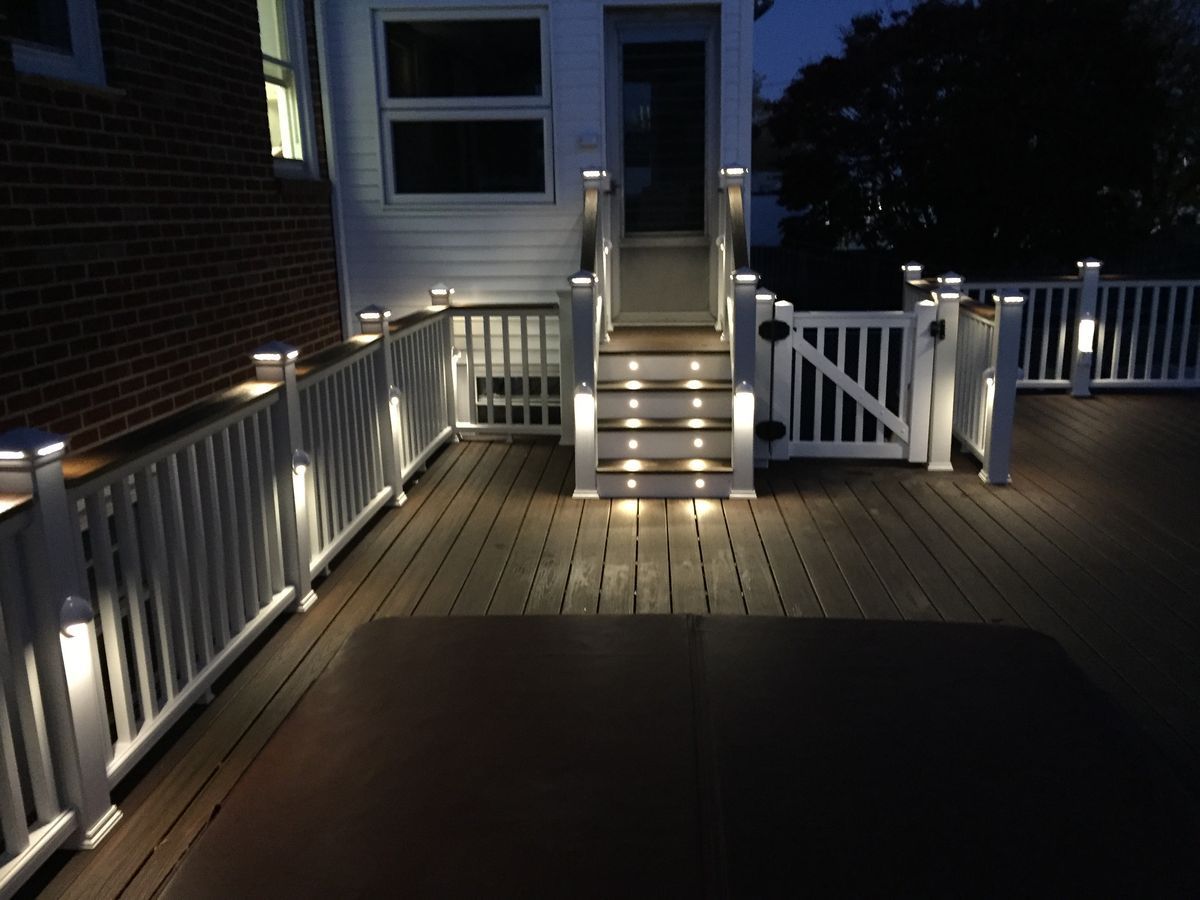 Lit deck at dusk with lights on railings and steps, leading to a doorway.