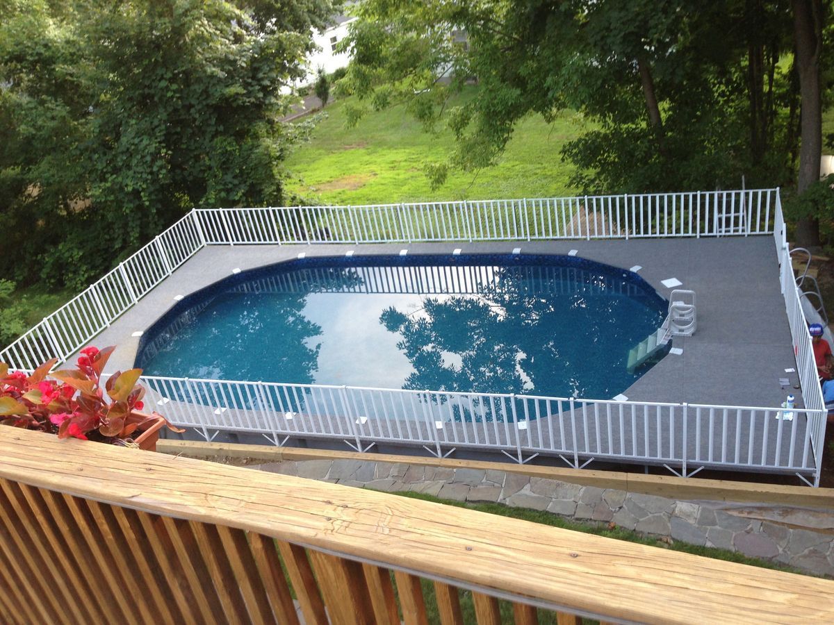 Above-ground oval pool surrounded by a white fence and a gray deck, set in a backyard with greenery.