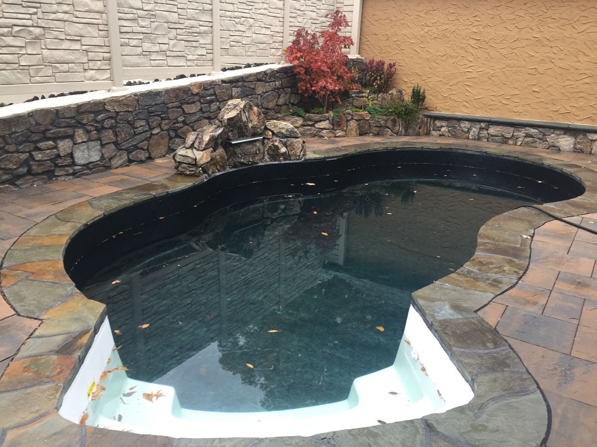 Pool, dark water, surrounded by stone and brick. Waterfall feature and fall foliage in background.