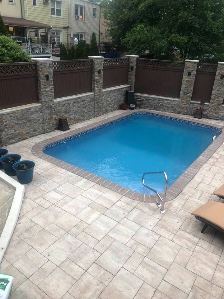 Night view of a house with a lit pool, outdoor seating, and surrounding trees under a cloudy sky.
