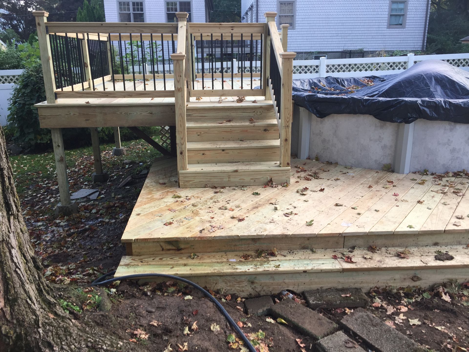 Wooden deck with stairs, black railing, beside a partially covered above-ground pool and white fence.