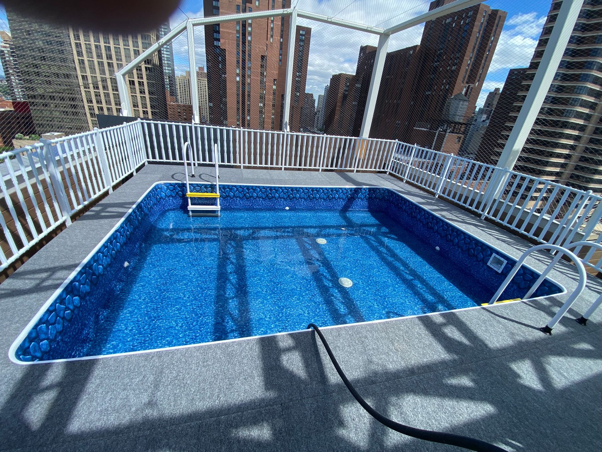 Night view of a swimming pool surrounded by a white fence and a deck with chairs.