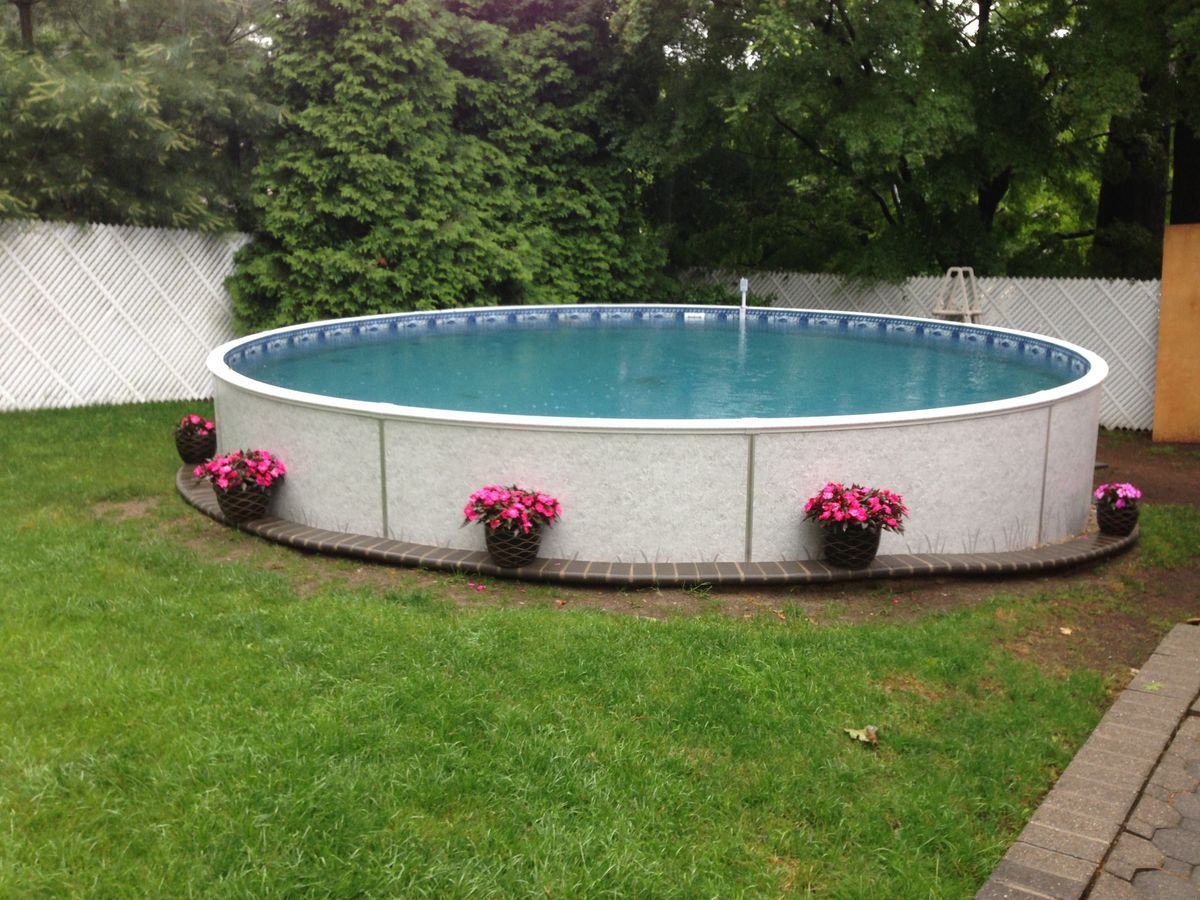 Round above-ground pool surrounded by green lawn, pink flowers, and white fence.