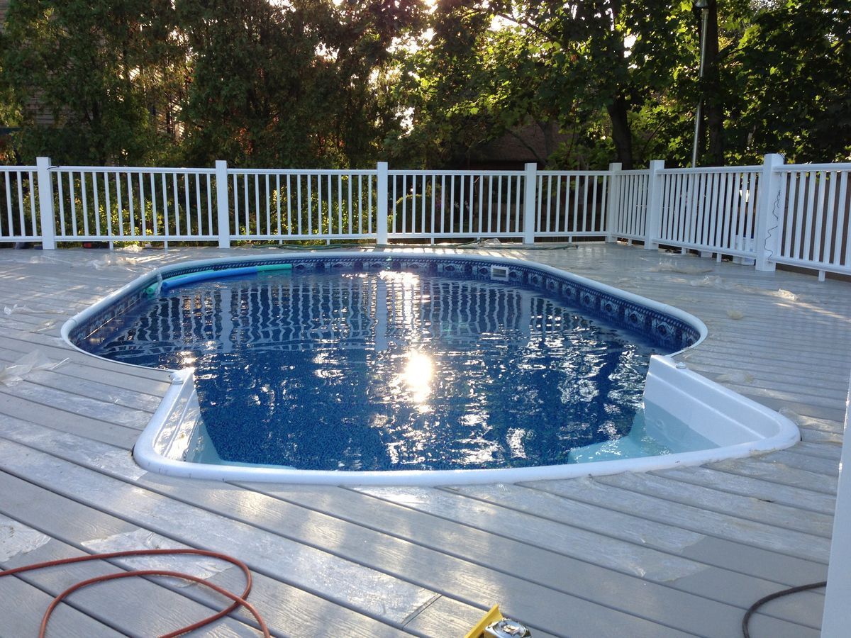 Above-ground swimming pool on wooden deck, surrounded by white fence. Sun reflecting on water.