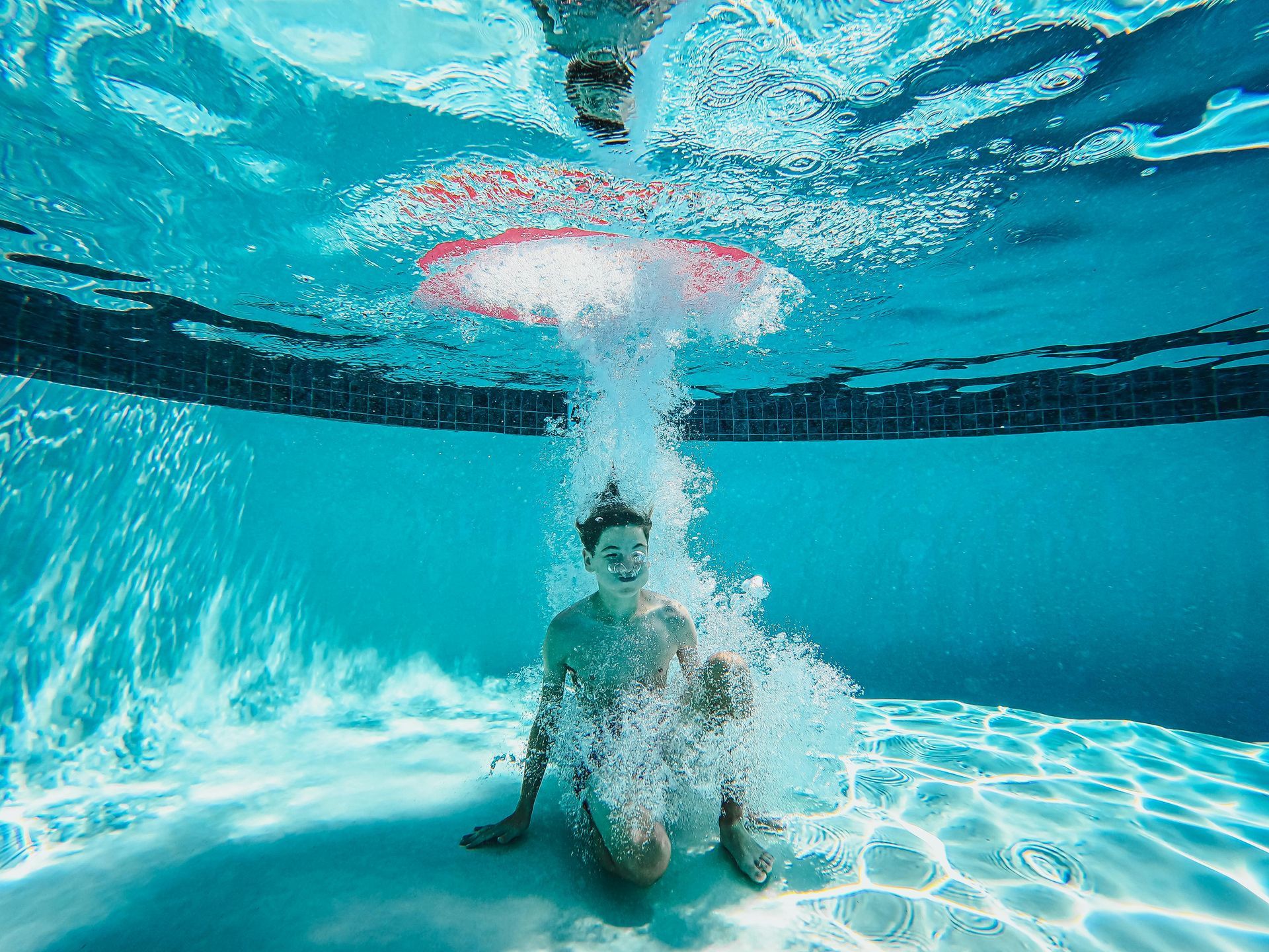 Underwater view of a person splashing in a pool, surrounded by bubbles.