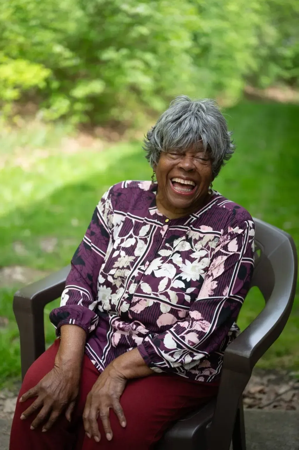 An elderly woman is sitting in a chair laughing.