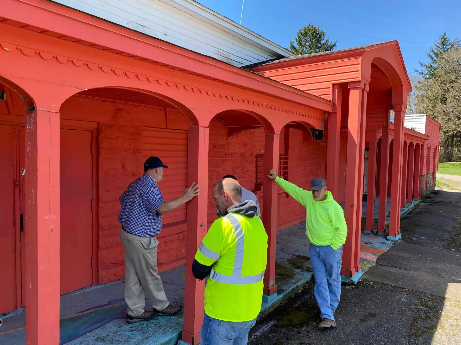 A group of men are standing in front of a red building.
