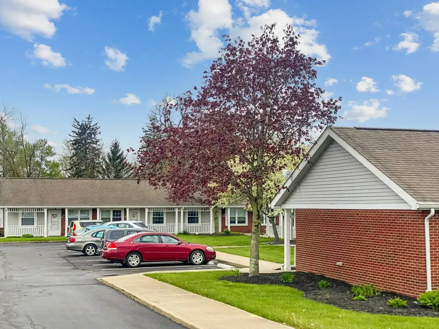A red car is parked in front of a brick house.
