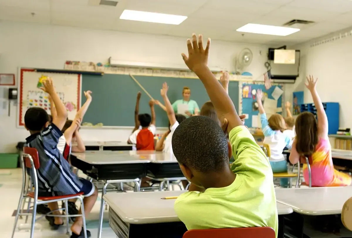 A group of children are raising their hands in a classroom