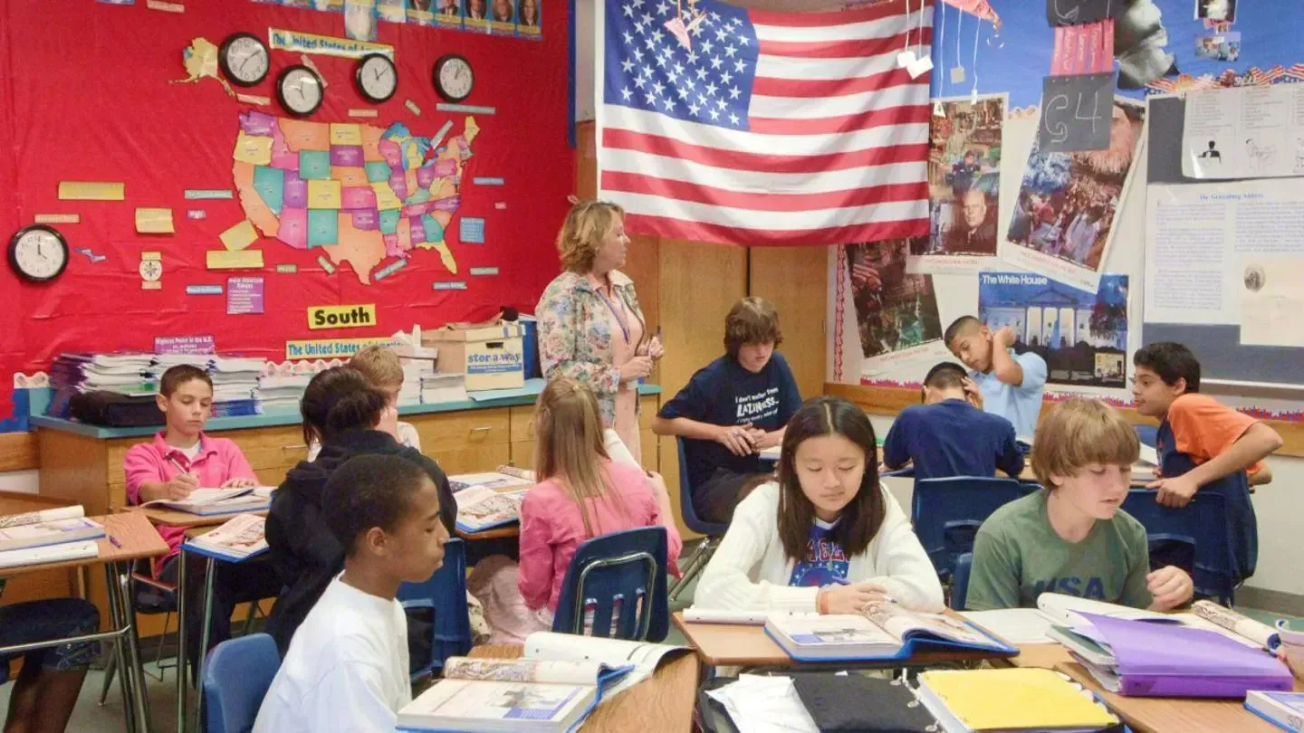 A group of children are in a classroom with an american flag on the wall