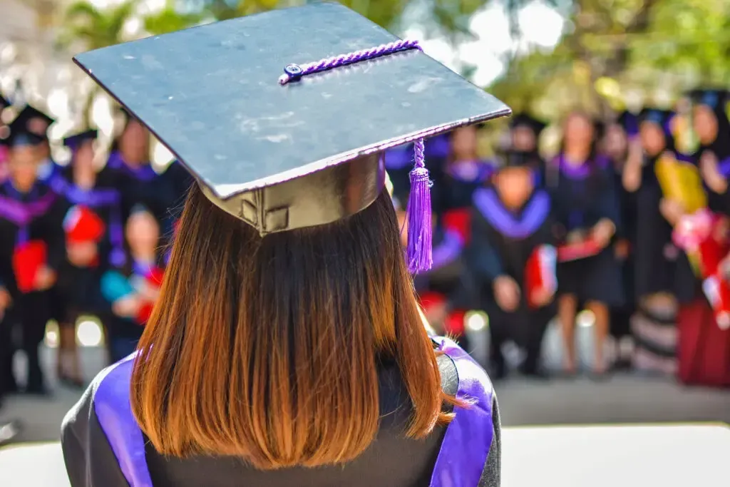 A woman wearing a graduation cap and gown is standing in front of a crowd of graduates.