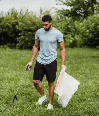 A man is picking up trash in a park.