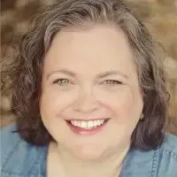 A woman is smiling for the camera and wearing a blue shirt.