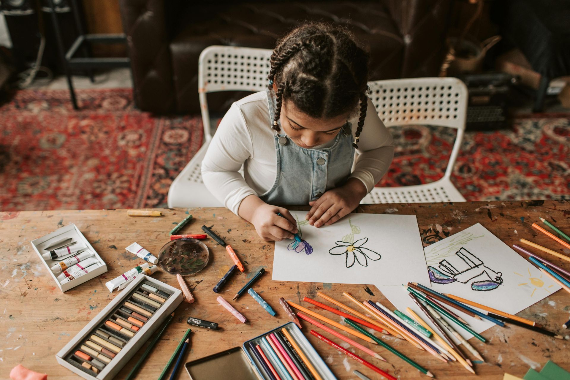A little girl is sitting at a table drawing with colored pencils