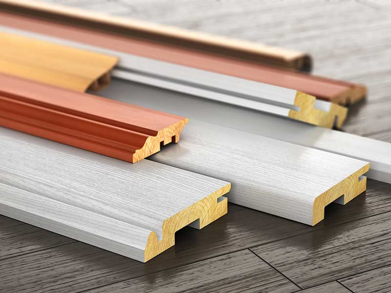 Wooden molding samples in various colors and designs on a wood floor.
