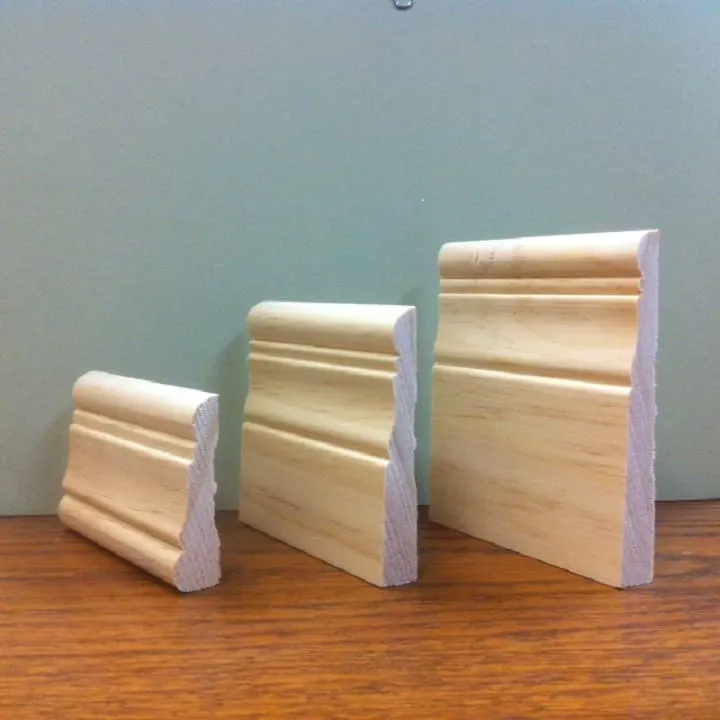 Three wooden molding samples of varying heights on a wood surface, against a green background.