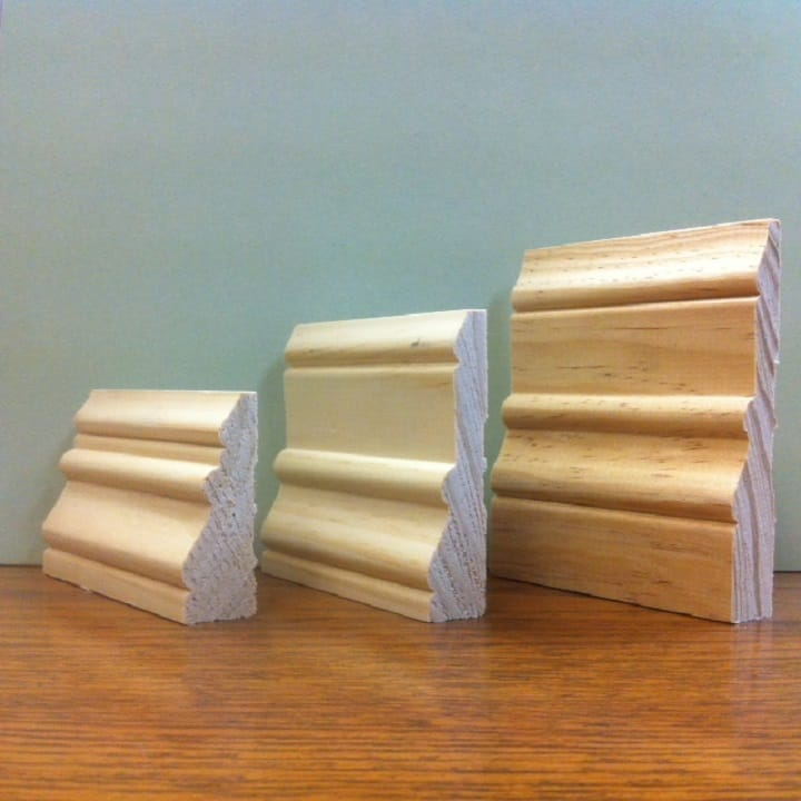 Three wood molding samples of varying sizes, displayed on a wood surface.