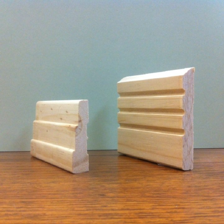 Two pieces of wooden trim molding on a wooden surface against a light green wall.