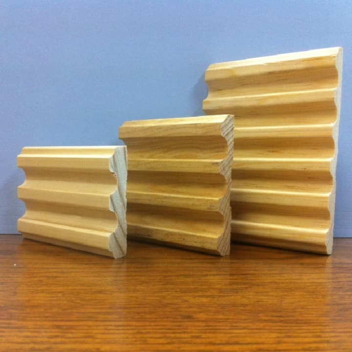 Three wooden decorative moldings with ridged profiles, displayed on a wood surface, against a blue background.
