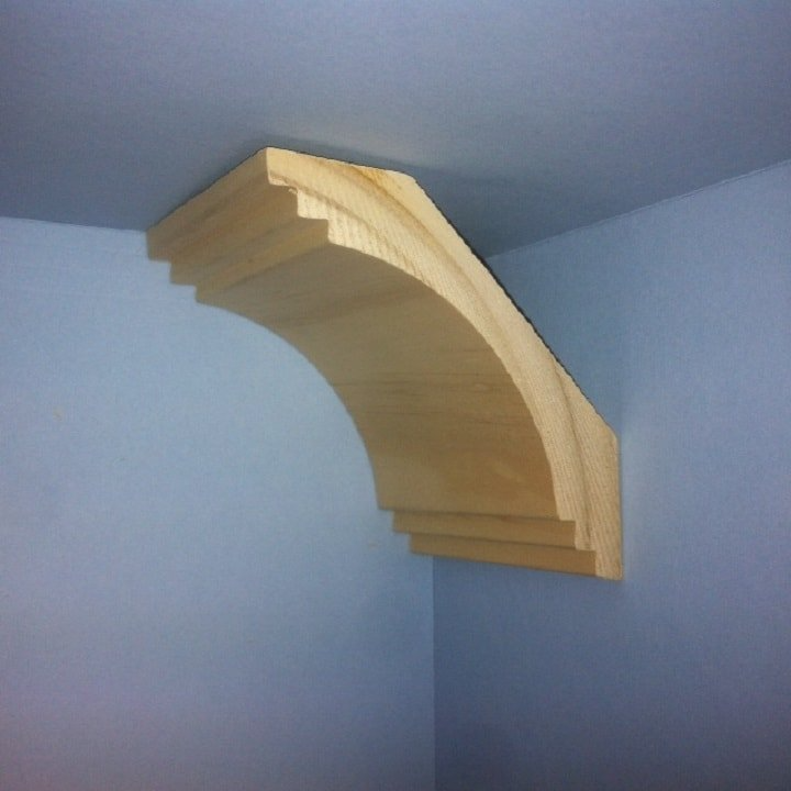 Wooden corbel mounted on a blue wall in the corner of a room, supporting the ceiling.