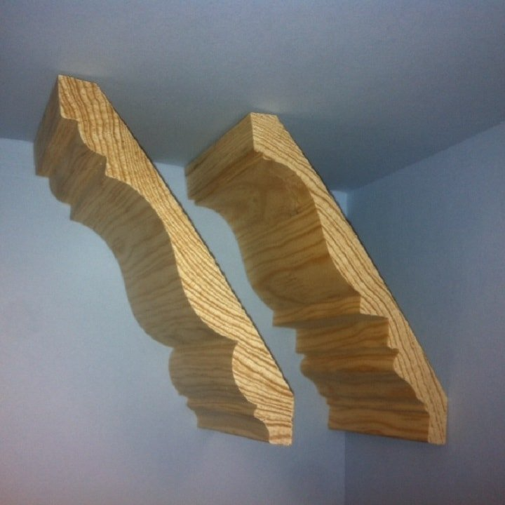 Two wooden corbels installed in a corner, showing decorative curves and grain.