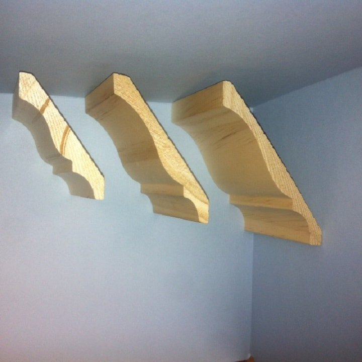 Three unfinished wooden crown molding samples mounted on a blue wall.
