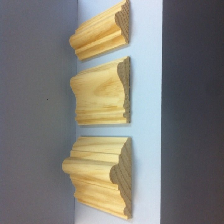 Three wooden crown molding samples displayed against a white and gray corner.