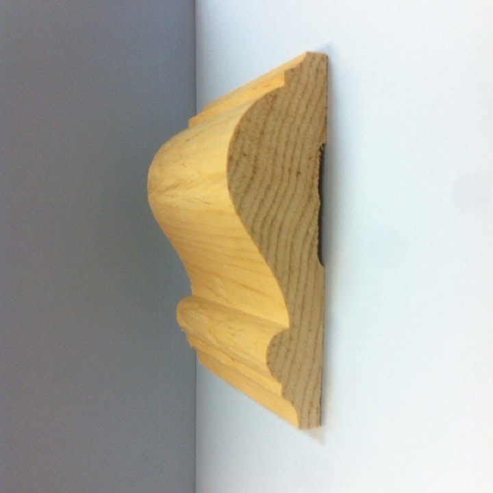 Wooden crown molding profile, natural wood color, mounted on a white wall.