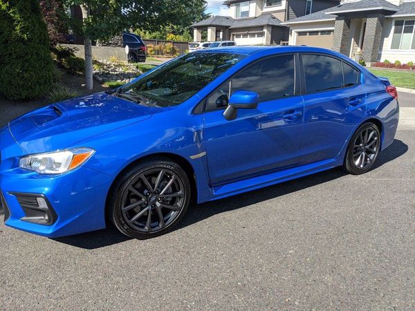 A blue subaru wrx sti is parked on the side of the road in front of a house.
