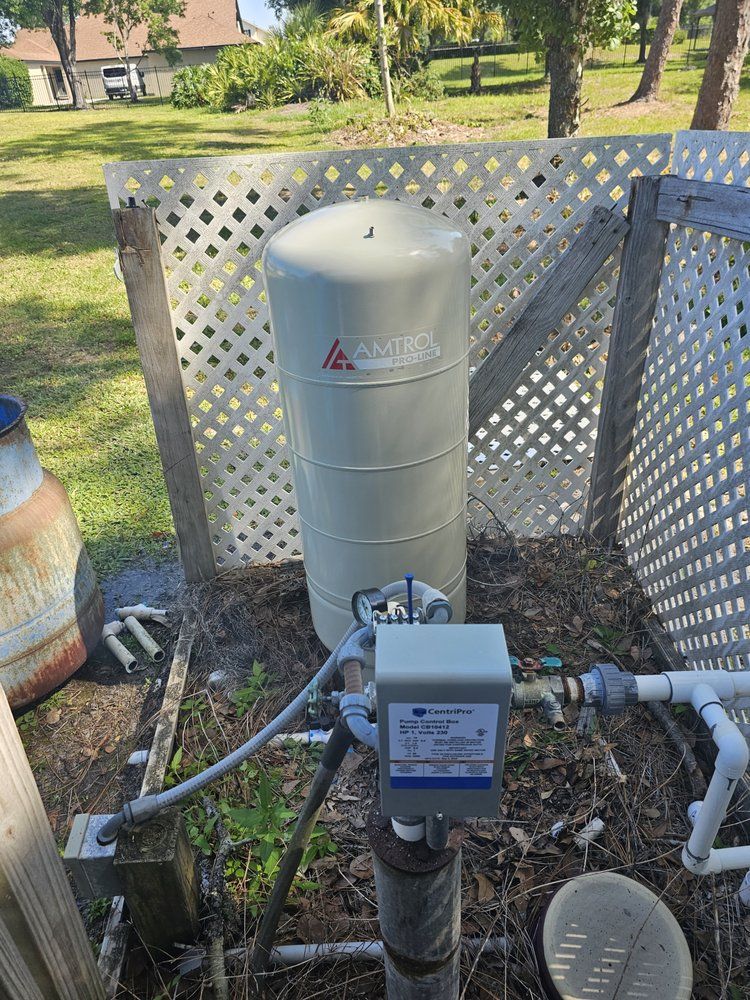 Water well equipment: beige tank, gray control box, set in a wooden lattice enclosure.