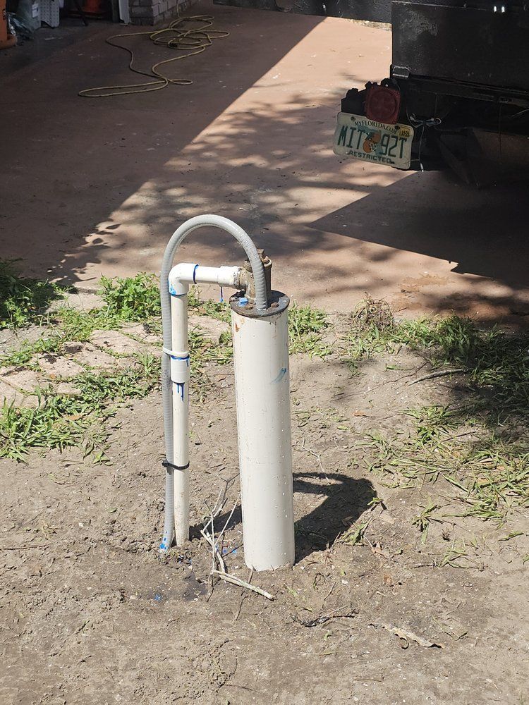 White well casing with PVC piping extending above ground in dirt.