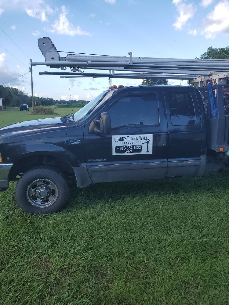 Black work truck with logo parked on grass, carrying pipes on roof rack.
