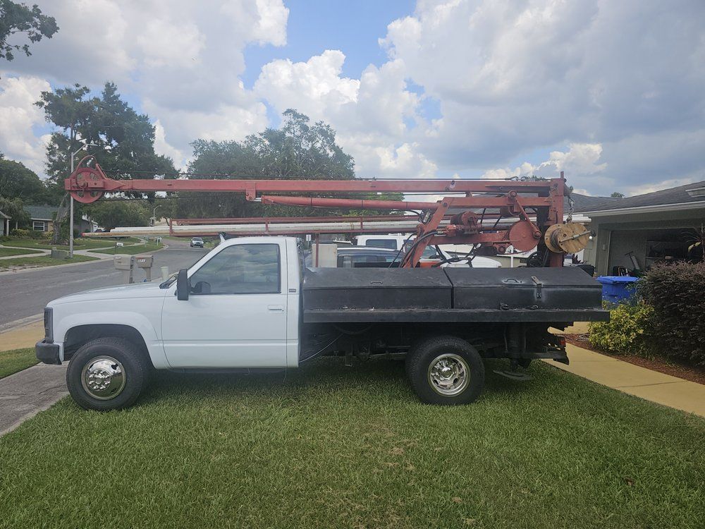 White flatbed truck with red machinery boom parked on grass next to a house.