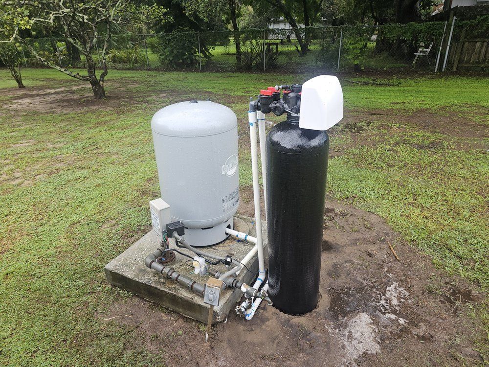 Well water system with pressure tank and filter on a concrete pad in a yard.