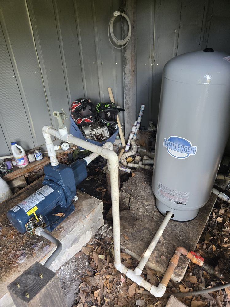 Well pump system with blue pump, gray tank, and white PVC pipes on wooden platform.