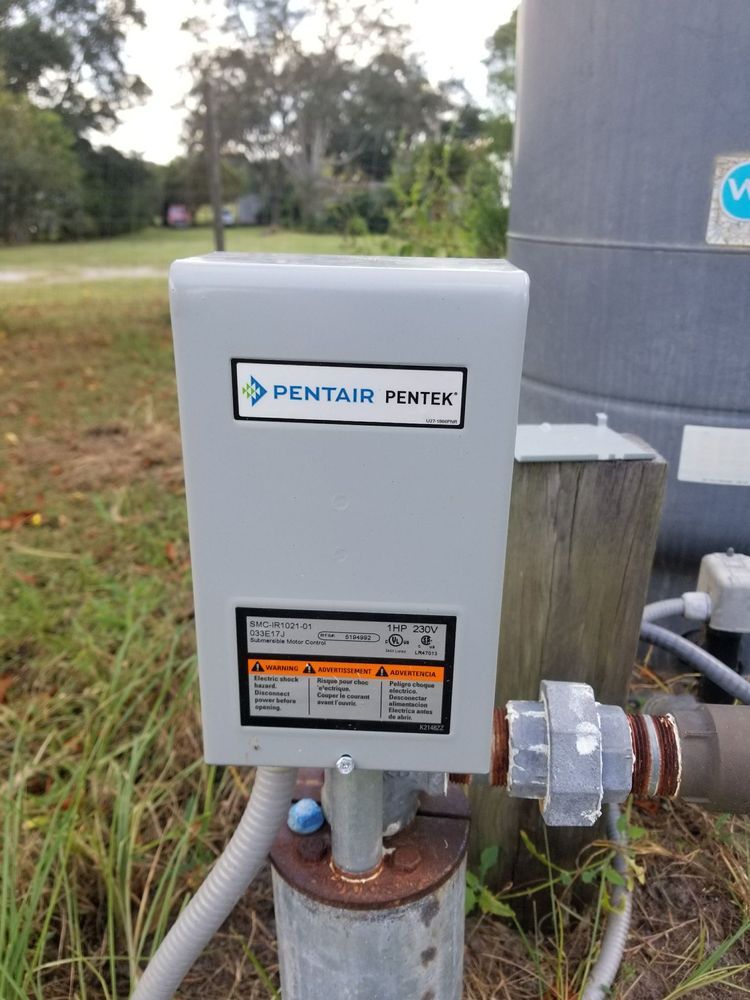 Gray Pentair electrical box on well pipe in grassy yard.