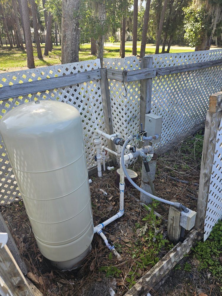 Water tank with pipes and valves by a white lattice fence.