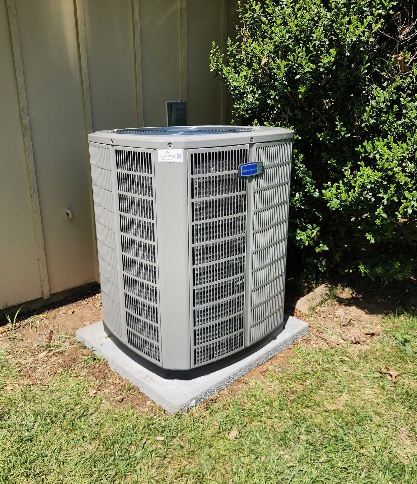 A large air conditioner is sitting on top of a concrete base in the grass.