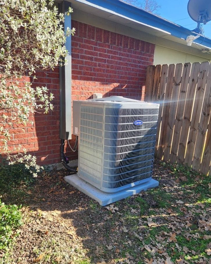 A carrier air conditioner is sitting outside of a brick house next to a wooden fence.
