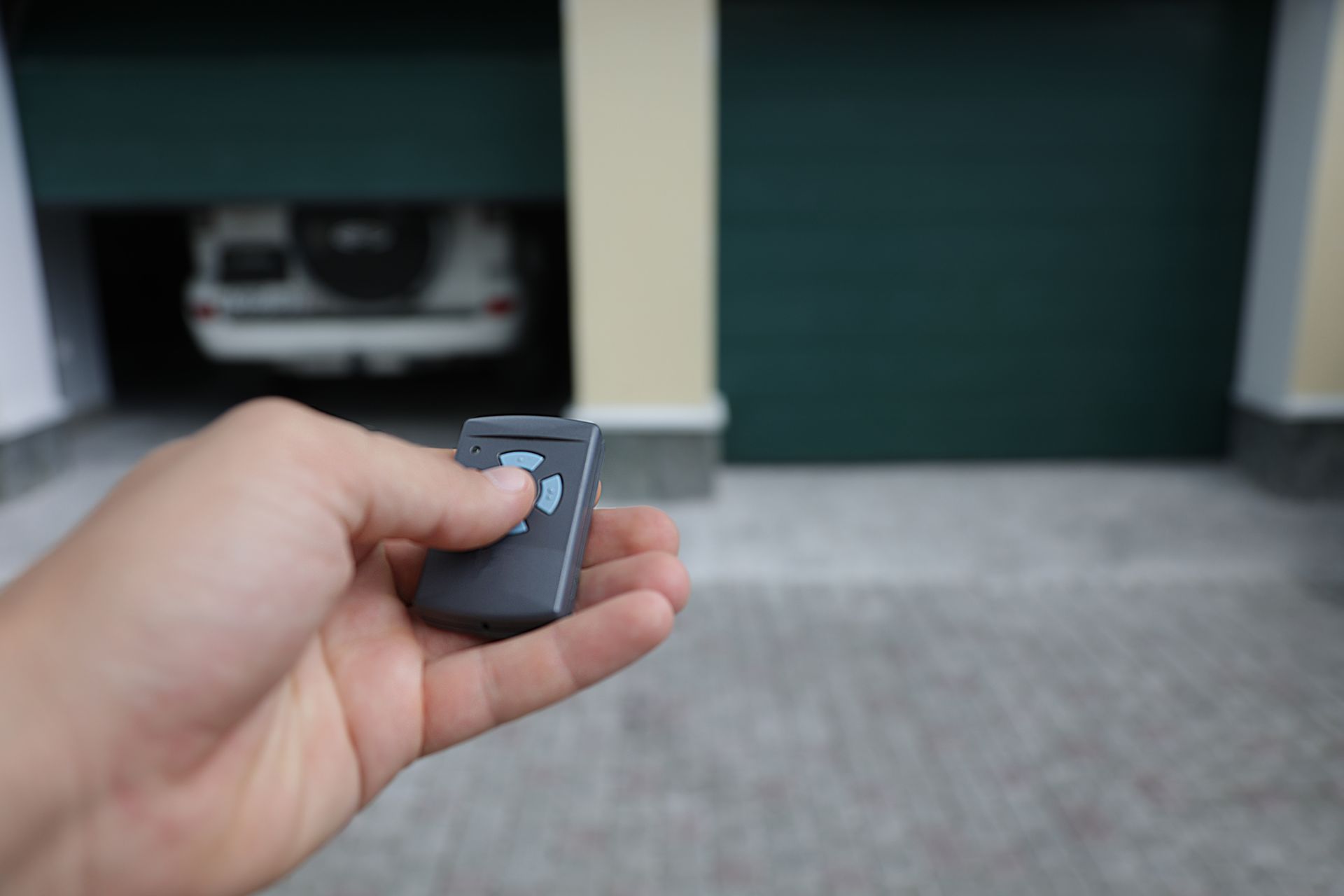 A person is holding a remote control in front of a garage door.