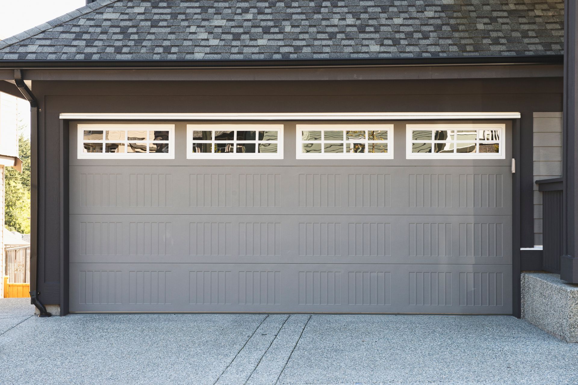 A gray garage door with white windows is sitting in front of a house.